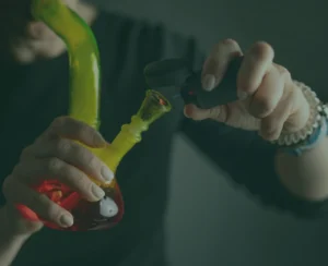 Burning and smoking hemp leaves from a bong flame closeup with female hands